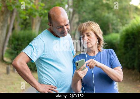 Mature adult couple strolling through the park while the woman shows the husband a photo on her mobile phone Stock Photo