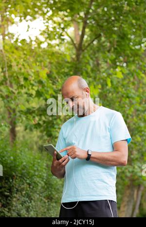 Man in sportswear and hairless walking through nature and consulting the route on his mobile phone Stock Photo