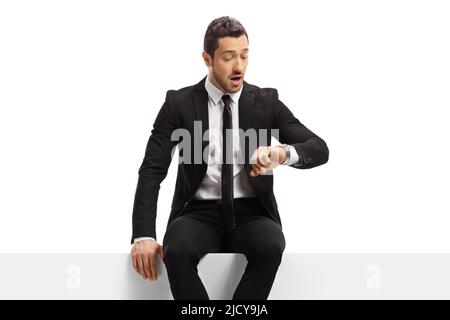 Surprised businessman sitting on a panel and checking time on his watch isolated on white background Stock Photo