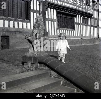 1940s, historical, a little girl by the steps outside the front of Bramall Hall, Bramhall, Stockport, England, UK. A timber-framed Tudor manor house that dates back to the 14th century, with later additions, the house and surrounding parkland was acquired by the local authority in 1935 and became a museum. The Davenport family, which it is believed built the house, held the manor for over 500 years. Stock Photo