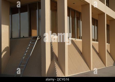 Dubai, UAE: corner of a minimalist and generic yellow office building with pillars, windows, and a ladder. Has pleasing lines, textures, and shapes. Stock Photo