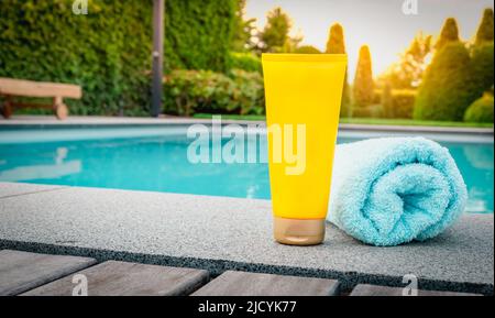 Skin care and protection against harmful sun rays. Yellow tube of sunscreen at the swimming pool. Stock Photo