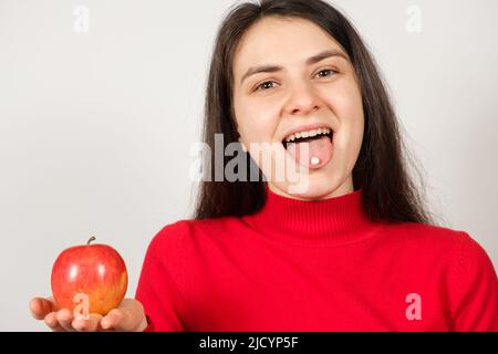 A woman with a pill on her tongue holds a red apple on a white background Stock Photo