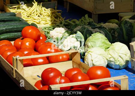 Red ripe organically grown tomatoes, green cucumbers for salad, young cabbage, yellow beans and cauliflower on a stall at a street market Stock Photo