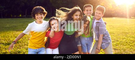 Happy childhood girls and boys from elementary school who play and frolic with friends in sunny park Stock Photo