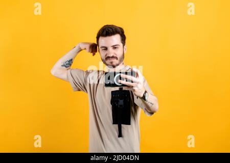 Handsome young man wearing casual clothes posing isolated over yellow background taking selfie, showing strong arm, flexing biceps and posing for phot Stock Photo