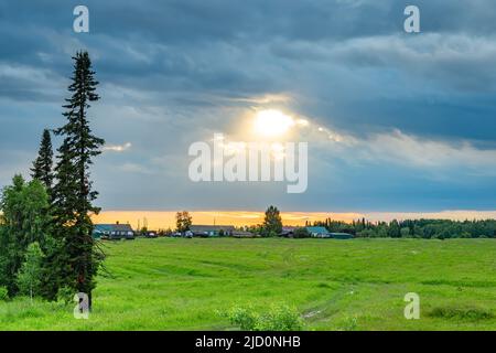 view of village houses against the background of the bright sun shining through the gloomy rainy clouds Stock Photo