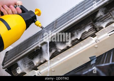A man washes off a special foam for cleaning air conditioners with a jet of water under pressure. Split system maintenance. Stock Photo
