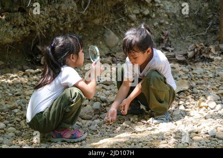 Asian tourist family, two sisters studying rocks with a magnifying glass as they travel to Pha Chor is high soil canyon cliffs at Mae Wang National pa Stock Photo