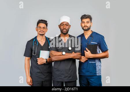 attractive medical team standing together over light gray background. African American nurse and two Indian doctors Stock Photo