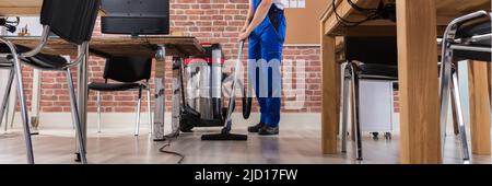 Happy Male Janitor Cleaning Floor With Vacuum Cleaner At Workplace Stock Photo