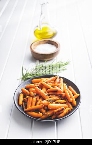 Roasted baby carrots with salt and rosemary on plate on white table. Stock Photo