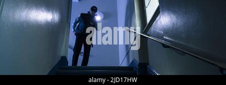 Male Security Guard Searching On Stairway With Flashlight Stock Photo