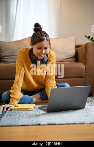 Cheerful young asian female relaxes sits in the living room and using portable notebook laptop computer. Stock Photo