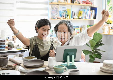 Cheerful and happy asian aged woman and young woman painting a ceramic cup together in the pottery workshop. Stock Photo