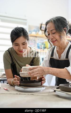 Aged asian woman and young asian woman making a ceramic cup together in the creative handicraft workshop. Stock Photo