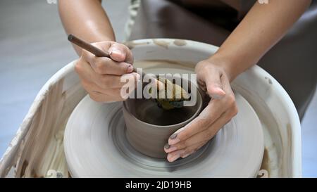 A female hands using a scrapper, making a ceramic cup on potter's wheel. Artisan production. cropped image Stock Photo