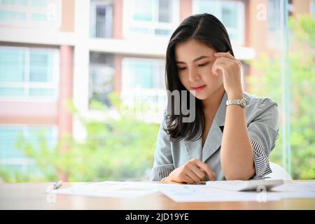 Attractive young Asian businesswoman or female entrepreneur concentrated reading a business document report. Stock Photo