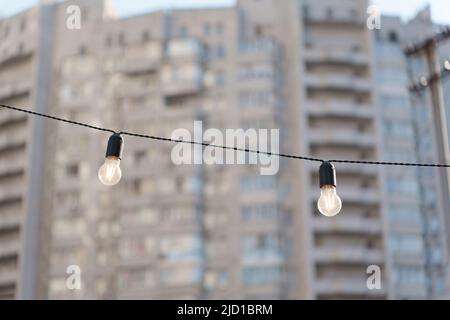 Two glowing light bulbs on a wire with a residential building background. Street lighting modernization concept. Stock Photo