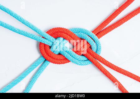 Red and blue cords intertwined in the shape of an infinity sign on a light gray background. Unity concept. Stock Photo