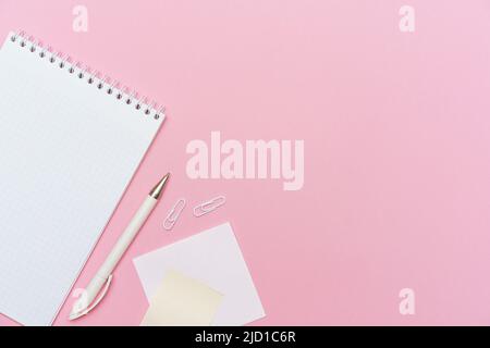 Workspace concept for school or office. Flat lay with an open notebook on a spring, a white color pencil, a plastic clip on paper background colors pink with copy space. Stock Photo