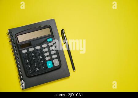 Notepad on spring black calculator and ballpoint pen on yellow background, business and accounting concept Stock Photo