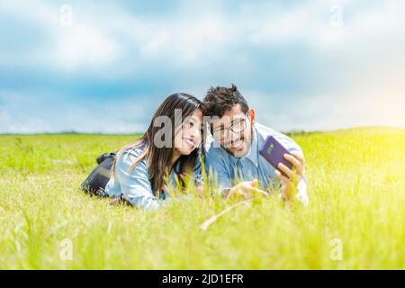 A couple lying on the grass taking a selfie, young couple in love lying on the grass taking a selfie, two people in love lying on the grass taking Stock Photo