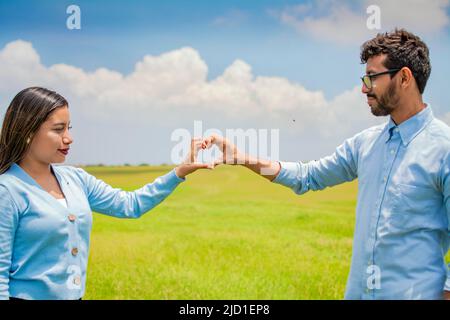 Happy couple making a heart shape with their hands, couple in love in the field making a heart shape with hands, beautiful couple in the field making Stock Photo