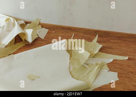 Torn pieces of old yellow striped wallpaper thrown on brown wooden floor in empty room. Scraps, rags, home redecoration. Stock Photo