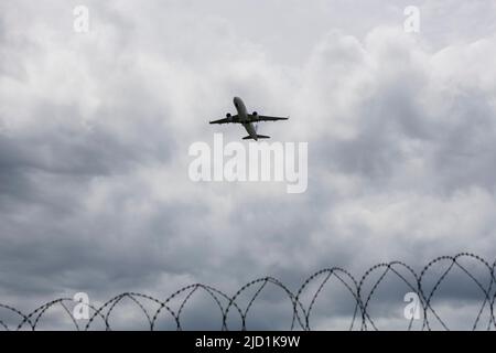 Aircraft taking off against a dark cloudy sky, security fence, barbed wire, Stuttgart, Baden-Wuerttemberg Stock Photo