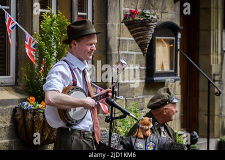 Haworth 1940 living history event (soloist performer, live music player, retro clothes, bunting, microphones) - Main Street, West Yorkshire England UK Stock Photo