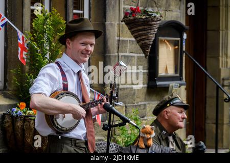 Haworth 1940 living history event (soloist performer, live music player, retro clothes, bunting, microphones) - Main Street, West Yorkshire England UK Stock Photo