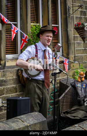 Haworth 1940 living history event (soloist performer, live music player, retro clothes, bunting, microphones) - Main Street, West Yorkshire England UK Stock Photo