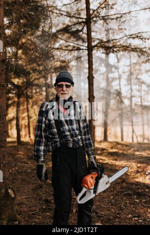 Senior man in forest holding chainsaw Stock Photo