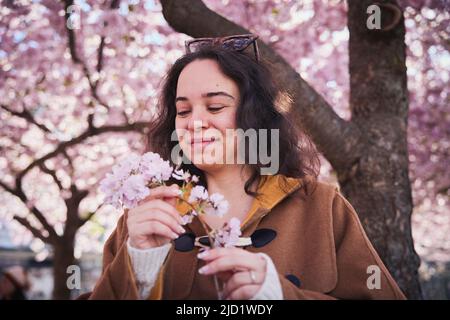 Young woman standing under cherry blossom and holding branch Stock Photo