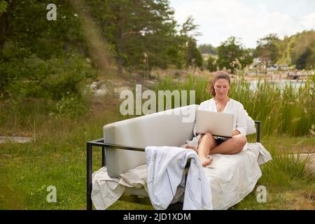 Woman using laptop on garden bench Stock Photo
