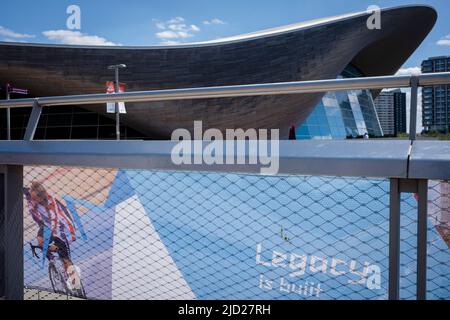 Ten years after the London 2012 Olympics were based here at Stratford, cyclist and multi-Gold medalist, Laura Trott appears on banners in The Queen Elizabeth Olympic Park, on 14th June 2022, in London, England. The former main Olympic venue area was controversially re-landscaped from an old industrial estate. Its promised legacy is a green space now known as The Elizabeth Park which remains a wildlife habitat and whose centrepieces are still the Velodrome and Aquatic Centre used by the public while the main Olympic statium is home to West Ham Football Club. Stock Photo