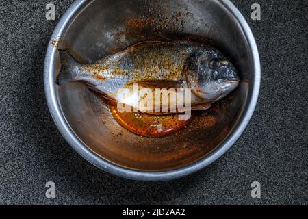 Ready to cook whole marinated sea bream in metal mixing bowl dish.Top view Stock Photo