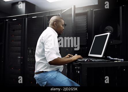 Making sure your servers are protected. Cropped shot of an IT technician using a computer while working in the server room of a data center. Stock Photo
