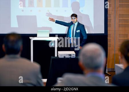 Making presenting look good. A handsome businessman gesturing while giving a presentation at a press conference. Stock Photo