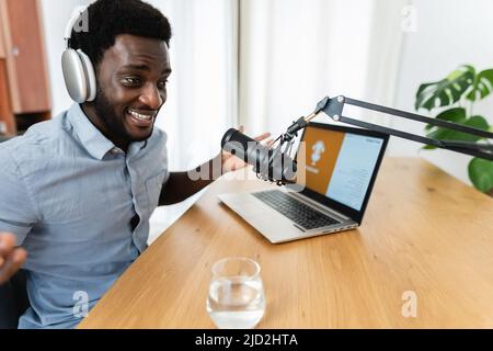 African man recording a podcast using microphone and laptop from his home studio Stock Photo