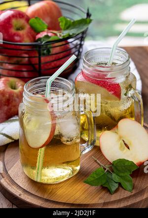 Two glasses of apple juice with apple slices and ice on a wooden platter with basket of apples in background Stock Photo
