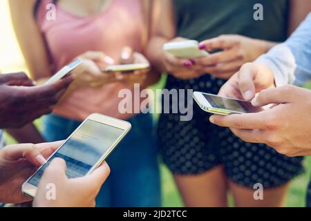 Mobile millennials. Cropped shot of a group of friends using their phones together outdoors. Stock Photo