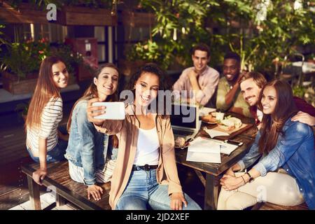 Im just here for the selfies. Cropped shot of an attractive young woman taking a selfie while out for lunch with friends. Stock Photo