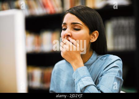 The student life isnt all that easy to keep up with. Shot of a university student yawning while working on a computer in the library at campus. Stock Photo