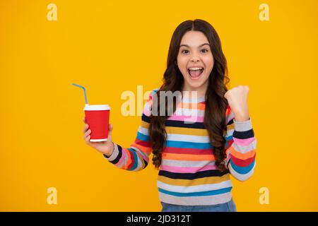 Amazed teenager. Teenage girl with take away cup of cappuccino coffee or tea. Child with takeaway cup on yellow background, morning drink beverage Stock Photo