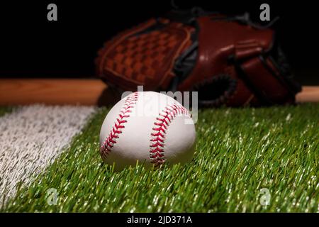 Baseball on grass field low angle close up with mitt and bat soft focus behind Stock Photo