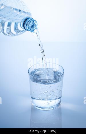 Pouring water from the bottle in to the glass isolated on blue background. Vertical format. Stock Photo