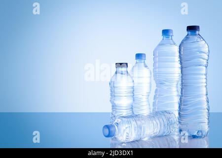 Plastic bottles of different sizes with mineral water isolated on blue background with copy space. Stock Photo