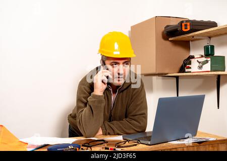 Contractor talking on cell phone with laptop in front of work office. Work organization concept, telecommunication, modern work. Stock Photo